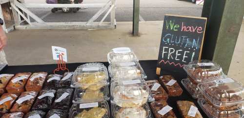 A market stall displaying various baked goods with a sign that says "We have GLUTEN FREE!" in colorful letters.