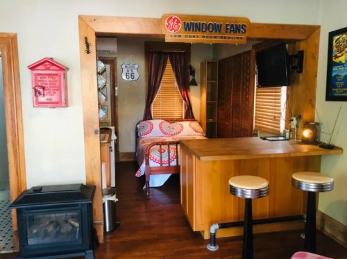 Cozy room with a bed, wooden bar, and vintage decor, featuring a window fan and a warm, inviting atmosphere.