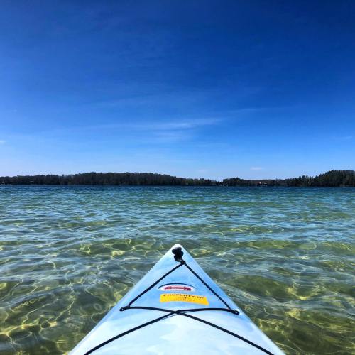 A kayak on clear water, with a blue sky and forested shoreline in the background.