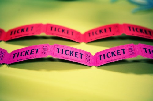A close-up of pink raffle tickets with the word "TICKET" printed on them, laid out on a bright yellow surface.