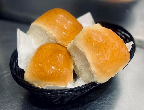 A black basket containing three shiny, golden-brown dinner rolls on white napkins.