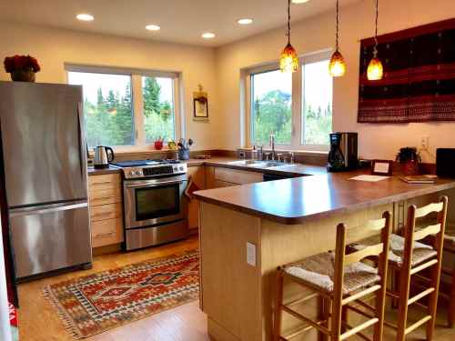 Bright kitchen with stainless steel appliances, wooden cabinets, and a cozy dining area featuring bar stools and a rug.