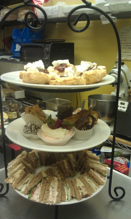 A tiered stand with assorted pastries, sandwiches, and desserts, displayed in a cozy kitchen setting.