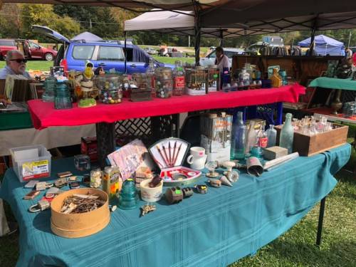 A vibrant market stall displaying various vintage items, including glass jars, tools, and collectibles on a green tablecloth.