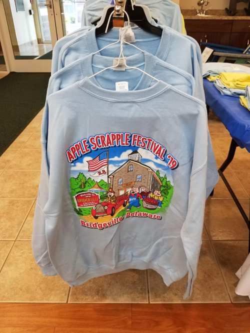 Light blue sweatshirts featuring a colorful design for the Apple Scrapple Festival 2019 in Bridgeville, Delaware.