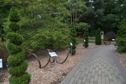 A winding path through a garden featuring topiary plants and informational signs among lush greenery.