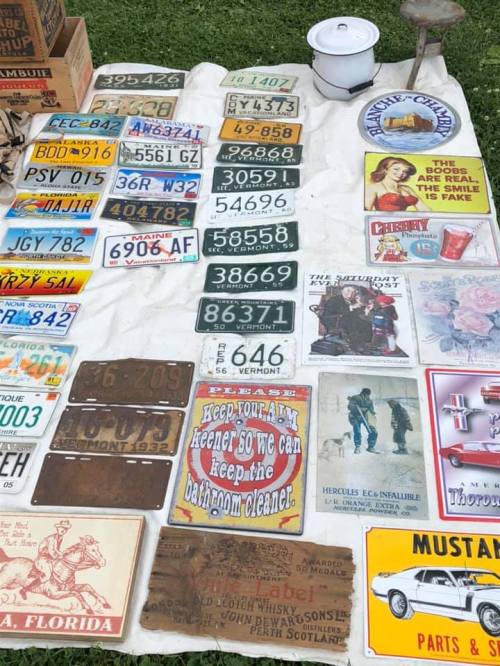A collection of vintage license plates and signs displayed on a white cloth outdoors.