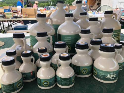 A collection of various sizes of Vermont maple syrup bottles displayed on a table at a market.