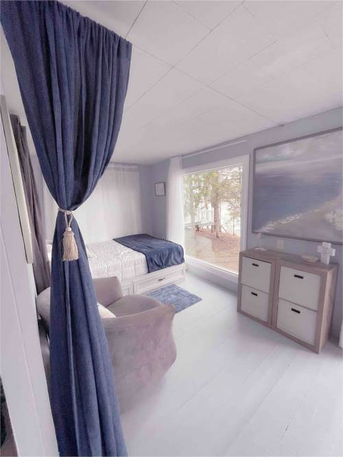 Cozy bedroom with a bed, large window, and curtains, featuring a serene view of nature outside.