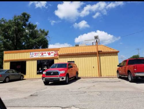 A yellow building with a metal roof, featuring two orange trucks parked outside under a blue sky with clouds.