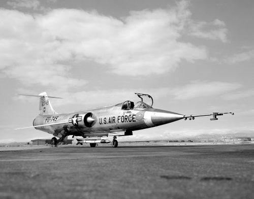 A U.S. Air Force fighter jet on a runway, with mountains in the background and a cloudy sky.