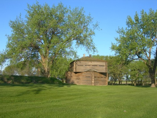A rustic wooden building surrounded by lush green grass and trees under a clear blue sky.