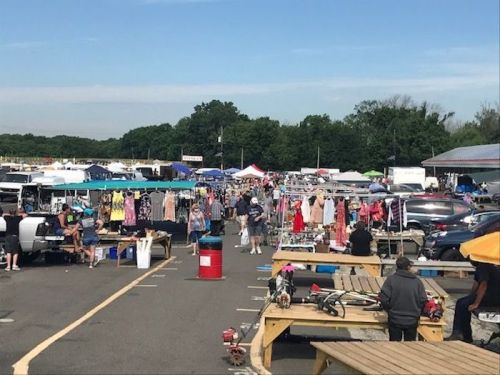 A bustling outdoor market with vendors, shoppers, and colorful tents under a clear blue sky.