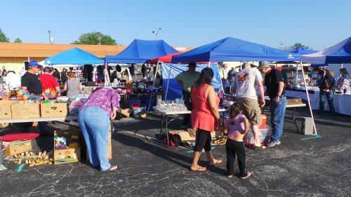 A bustling outdoor market with colorful tents, vendors, and shoppers browsing various goods on a sunny day.