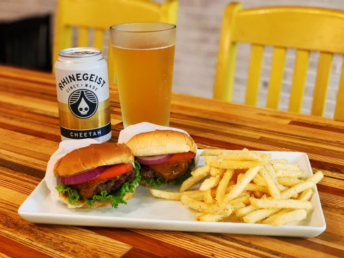 Two burgers with lettuce, tomato, and onion, served with fries and a can of beer on a wooden table.