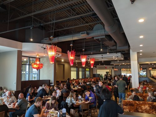 A busy restaurant interior with colorful pendant lights, filled with diners at tables and staff serving.