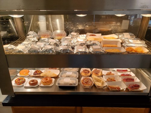 A display case filled with various baked goods, including pastries, donuts, and wrapped sandwiches.
