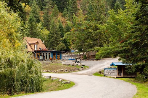 A scenic view of a winding road leading to a rustic lodge surrounded by trees in a mountainous area.