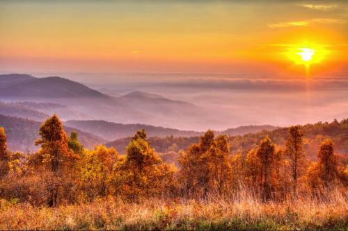 A vibrant sunset over rolling hills, with autumn foliage in the foreground and misty valleys in the background.