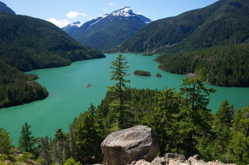 A scenic view of a turquoise lake surrounded by lush green forests and mountains under a clear blue sky.