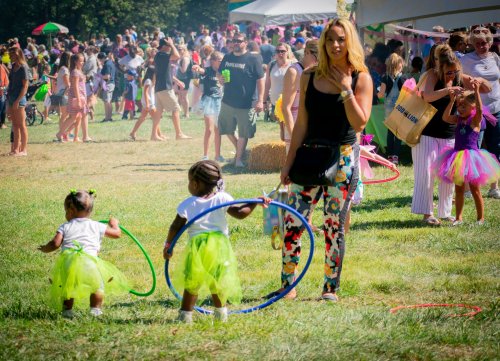 A woman watches two children in tutus playing with hula hoops at a crowded outdoor event.
