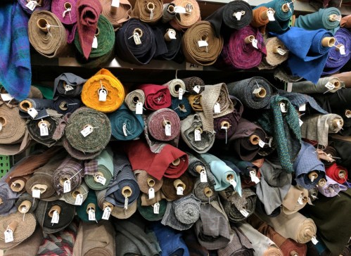 A variety of rolled fabrics in different colors and patterns, neatly organized on shelves with tags attached.