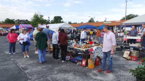 A bustling outdoor market with people browsing various stalls and tables filled with vintage items and crafts.