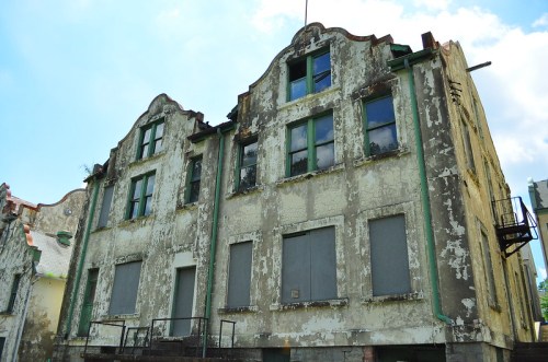 Abandoned building with peeling paint, boarded windows, and a distinctive architectural style under a blue sky.