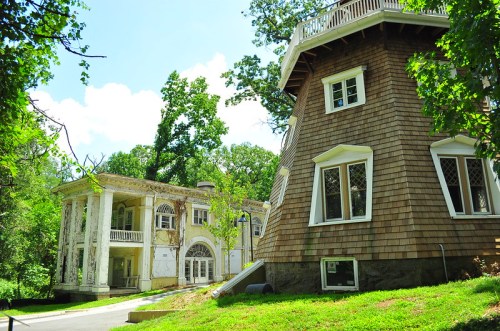 Two distinct buildings in a lush green setting: one is a weathered mansion, the other a unique, shingled structure.
