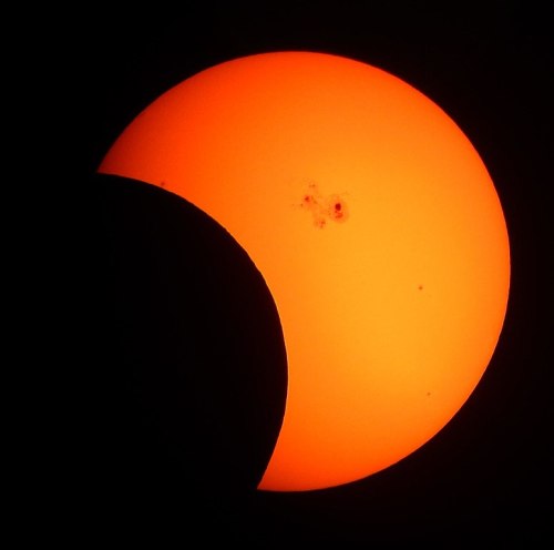 A partially eclipsed sun glowing bright orange against a dark background.