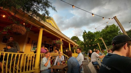 A lively outdoor gathering at a restaurant with string lights, people enjoying drinks, and a cozy atmosphere.