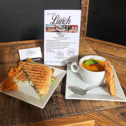 A sandwich with chips and a cup of soup on a wooden table, alongside a lunch special flyer.