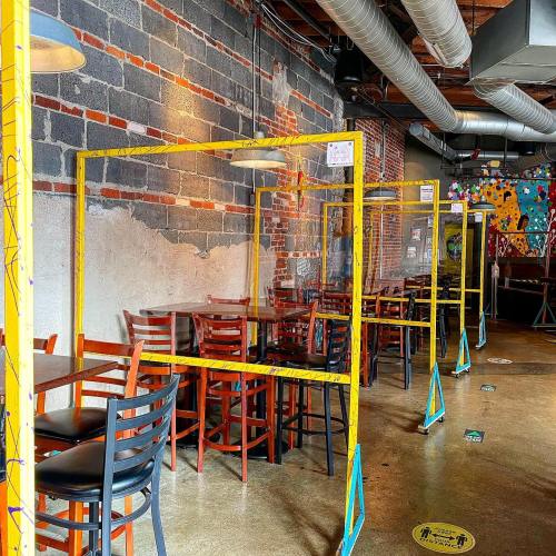 Interior of a restaurant with colorful partitions between tables, exposed brick walls, and a modern industrial design.