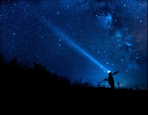 A silhouette of a person holding a telescope, pointing a beam of light at a starry night sky filled with the Milky Way.