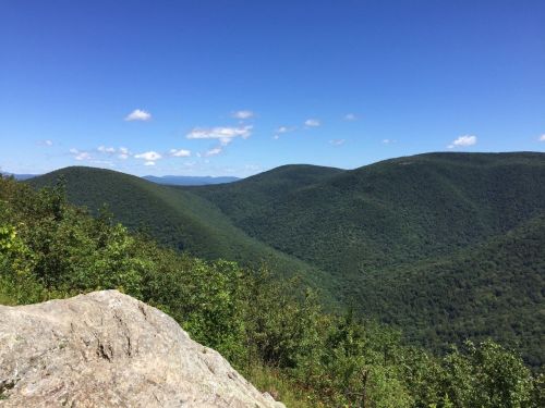A scenic view of rolling green mountains under a clear blue sky with a few clouds.