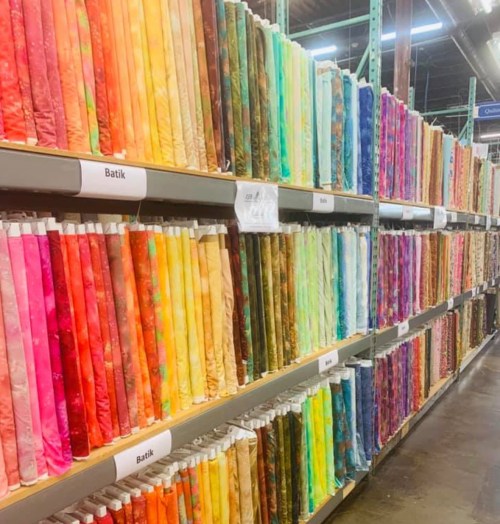 A colorful display of fabric rolls in various shades, organized neatly on shelves in a craft store.