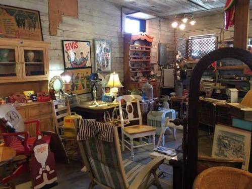 A cozy antique shop filled with vintage furniture, decor, and memorabilia, including a Santa figure and Elvis posters.