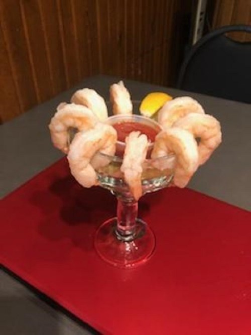 A glass filled with shrimp arranged around the rim, served with a lemon slice on top.