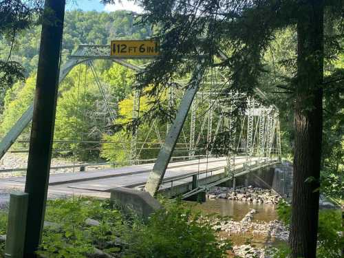 A green metal bridge spans a river, surrounded by trees, with a sign indicating a height limit of 12 feet 6 inches.