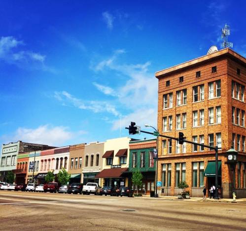 A charming downtown scene featuring historic brick buildings, shops, and a clear blue sky.