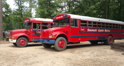 Two red school buses parked in a wooded area, labeled "Seminary Canoe Rental" with a stop sign on the front.