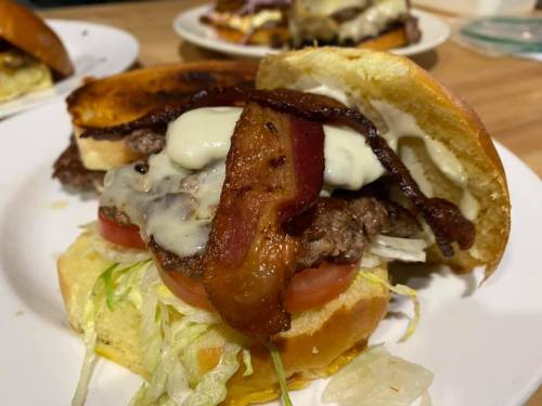 A close-up of a burger with a beef patty, bacon, cheese, lettuce, and tomato on a toasted bun, served on a plate.