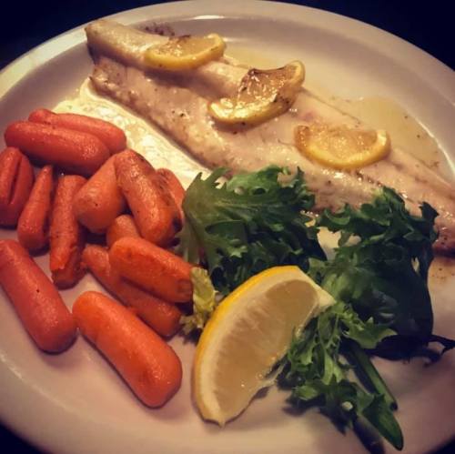 A plate featuring grilled fish with lemon slices, accompanied by sautéed carrots and a side of fresh greens.