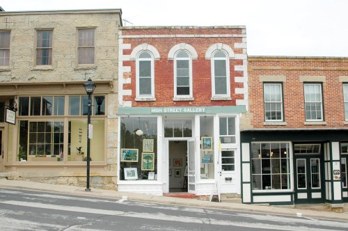 A quaint art gallery with a red brick facade, surrounded by historic buildings on a sloped street.