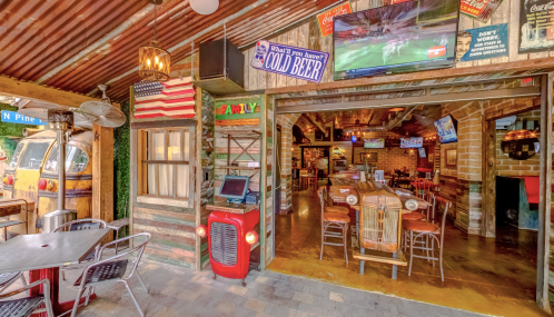 A rustic bar entrance with wooden decor, TVs, and a vintage red vehicle, inviting patrons to enjoy cold drinks.
