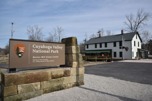 Sign for Cuyahoga Valley National Park in front of the Boston Mill Visitor Center, with a historic building in the background.