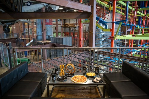 A cozy seating area with a table of pizza, pretzels, and snacks, overlooking a colorful indoor adventure park.