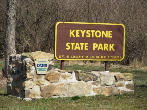 Sign for Keystone State Park, featuring stone base and yellow lettering, surrounded by trees and grass.