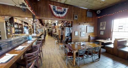 Interior of a rustic restaurant with wooden decor, tables, and a bar, featuring warm lighting and patriotic decorations.