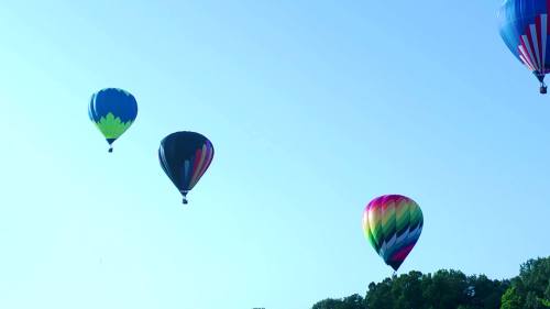 Three colorful hot air balloons float in a clear blue sky above a green landscape.